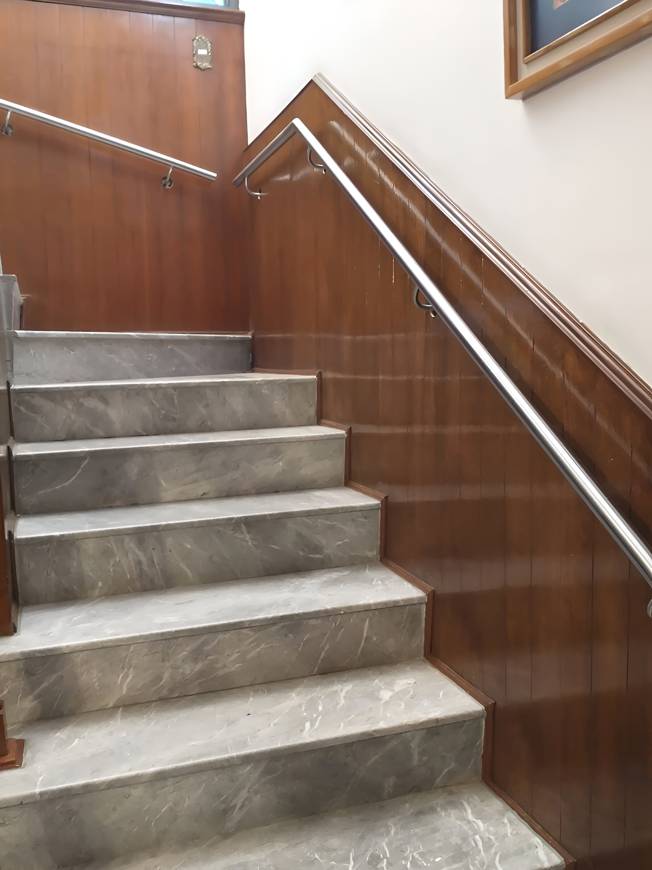 Pasamanos inox satinado montado en pared de madera junto a escalones de mármol