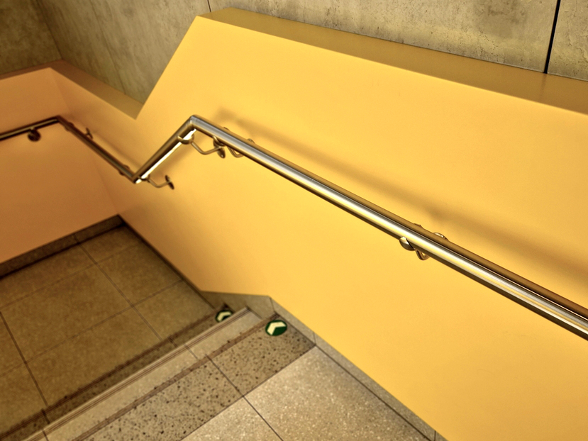 Pasamanos inoxidable continuo fijado a muro amarillo en escalera estrecha de vivienda